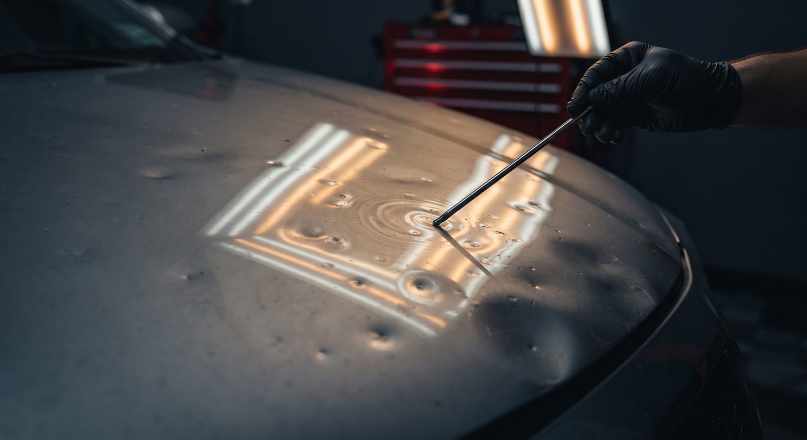 360 PDR technician reading hail dents on a vehicle hood with a PDR reflector board during a damage inspection